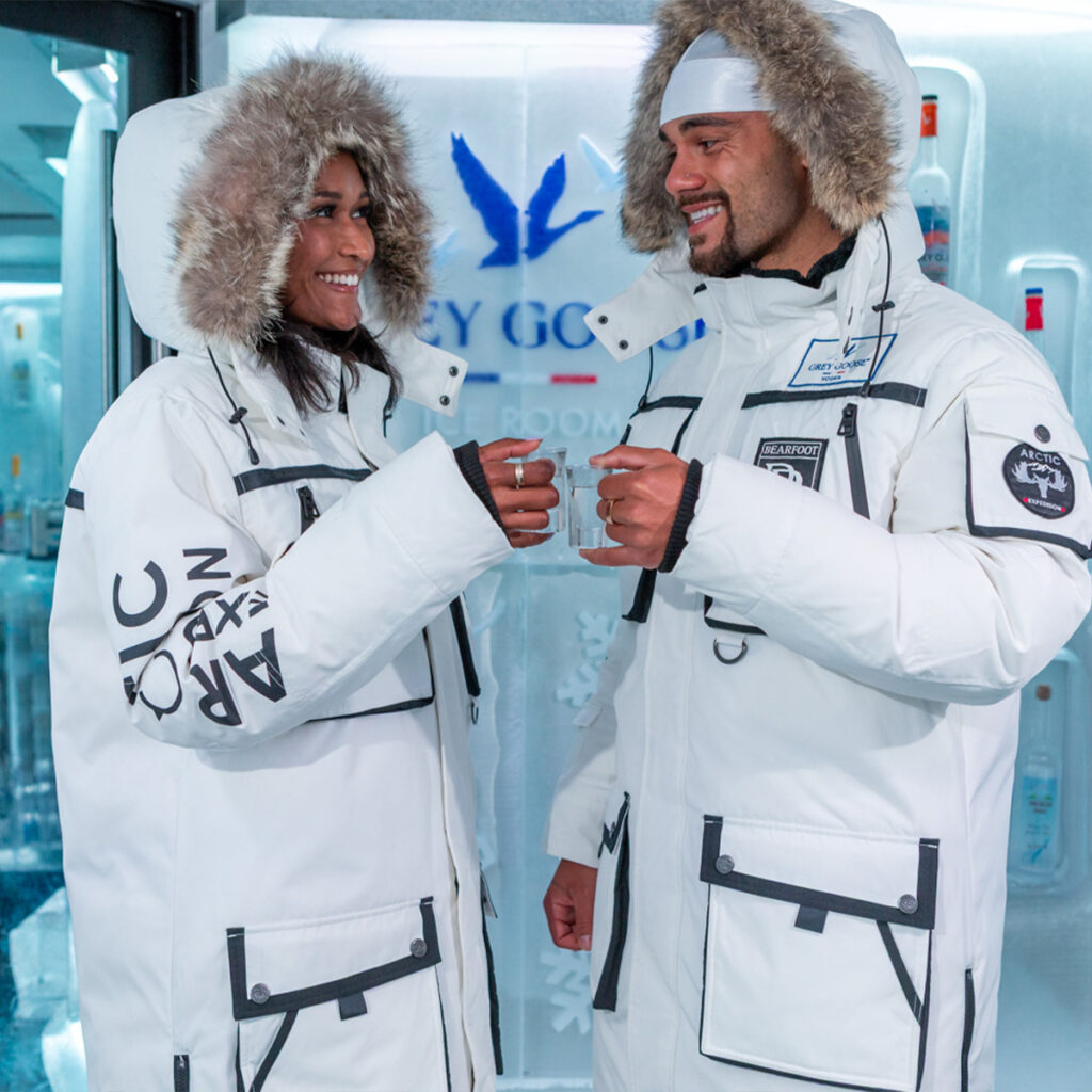 Guests wearing parkas posing with vodka shots alongside a host pouring Grey Goose inside the sub-zero Ice Room at Bearfoot Bistro.