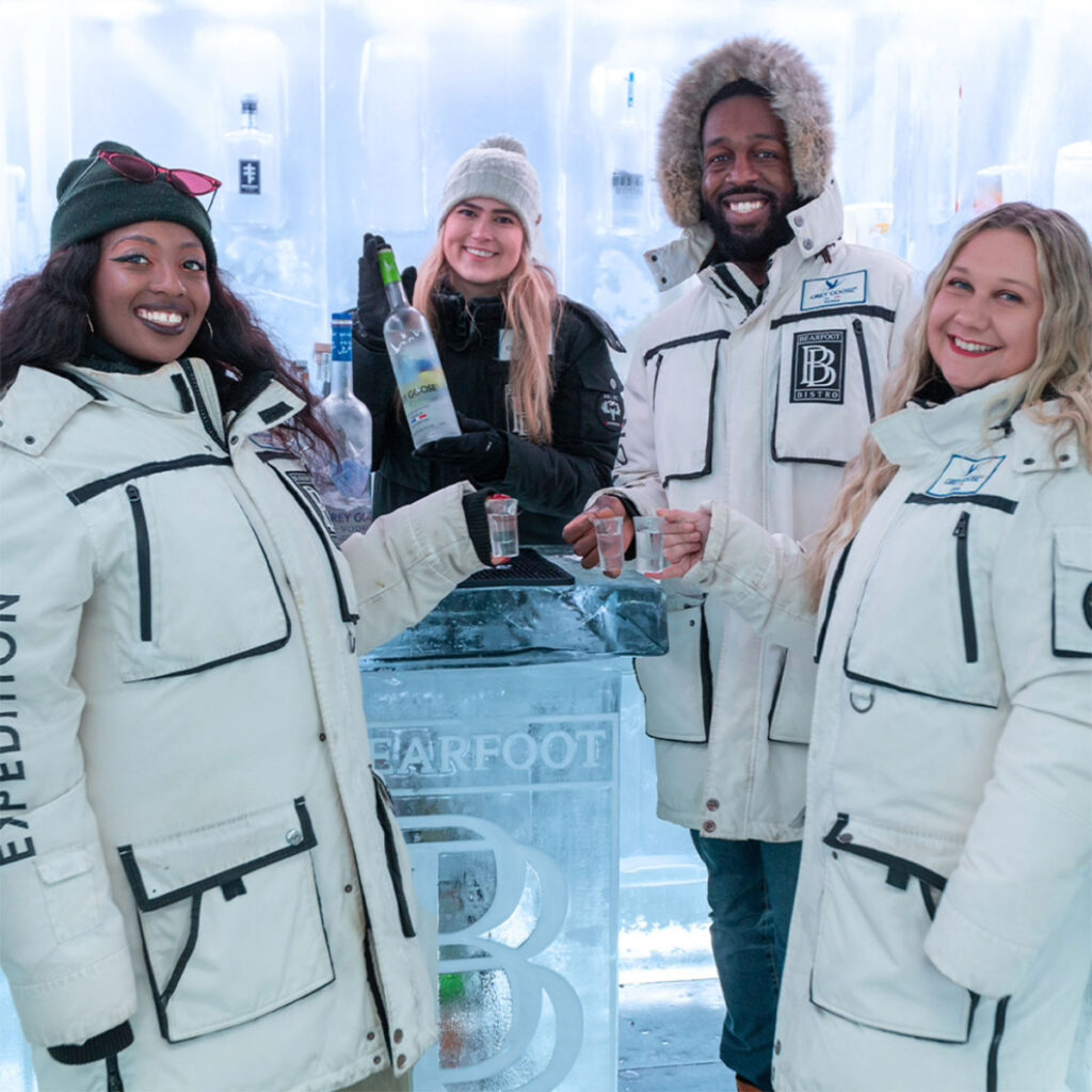 Guests wearing parkas posing with vodka shots alongside a host pouring Grey Goose inside the sub-zero Ice Room at Bearfoot Bistro.
